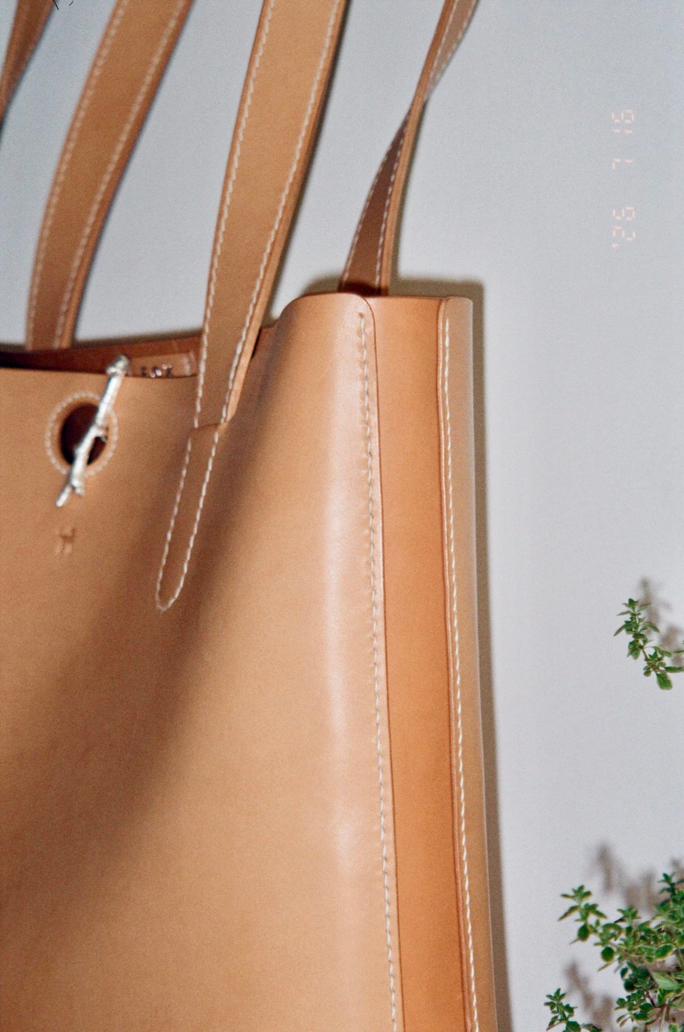 Close-up of a tan leather tote bag with double shoulder straps, showing the side seam
